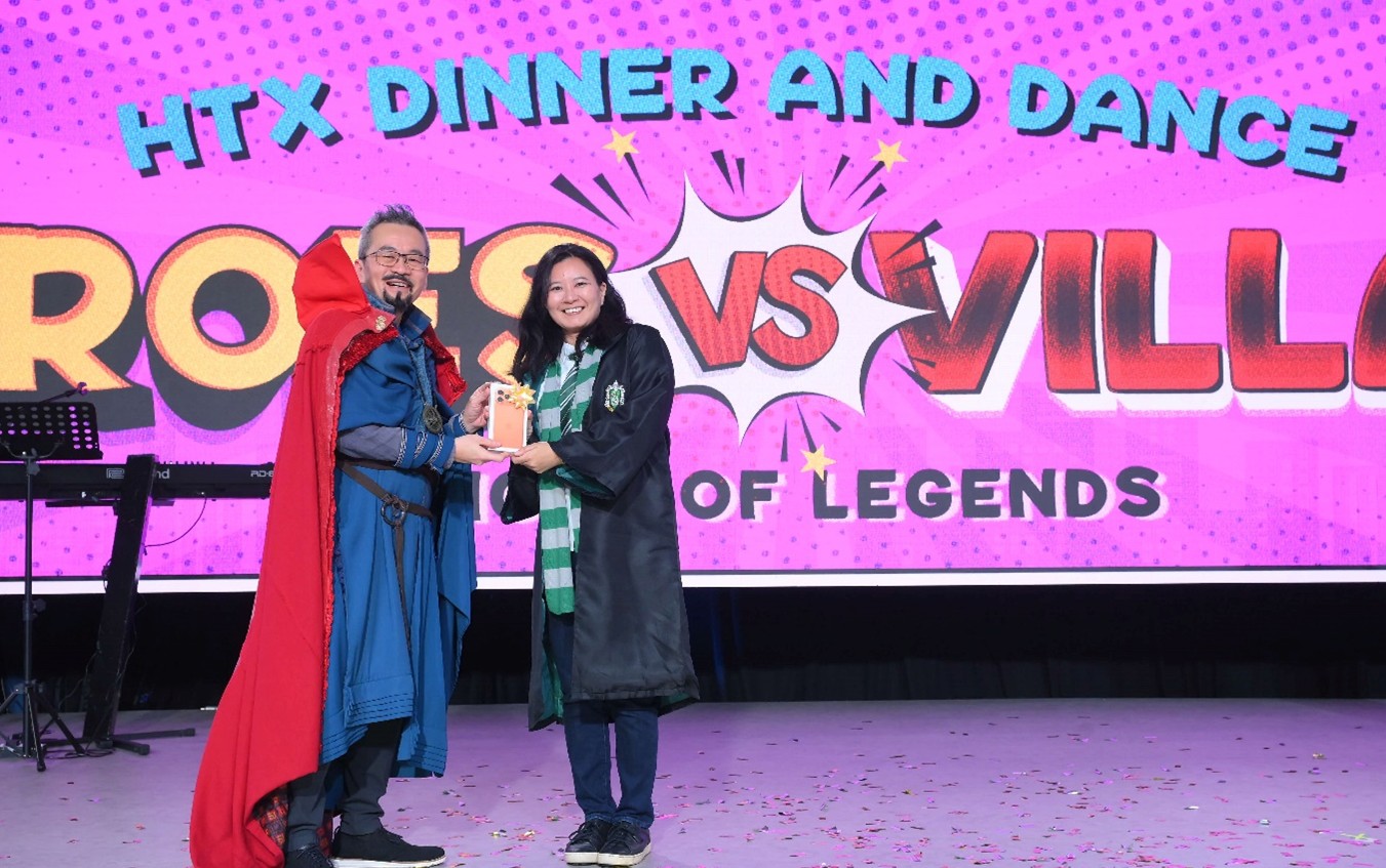 Two people in costumes pose on stage while holding a small box together.