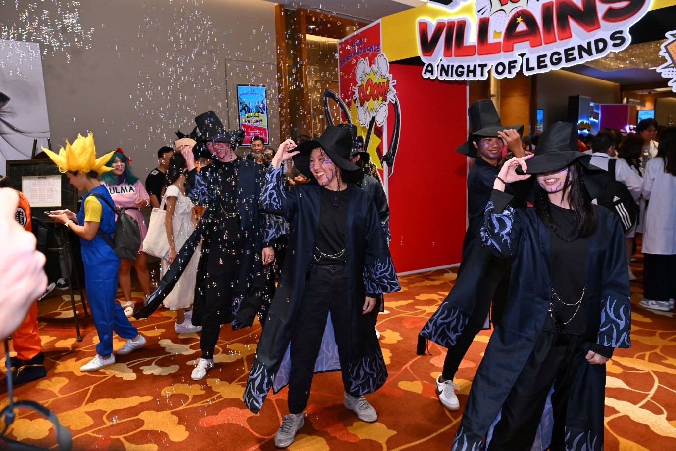 A group of people in dark robes and hats dancing as bubbles fall around them.