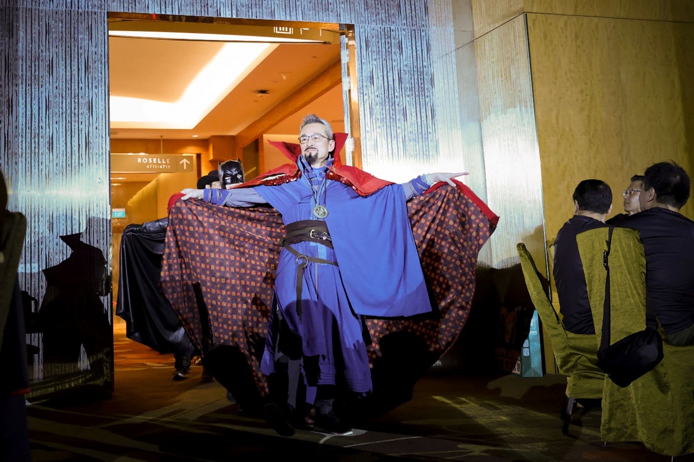 A person in a large cape enters a door holding the cape open out wide.