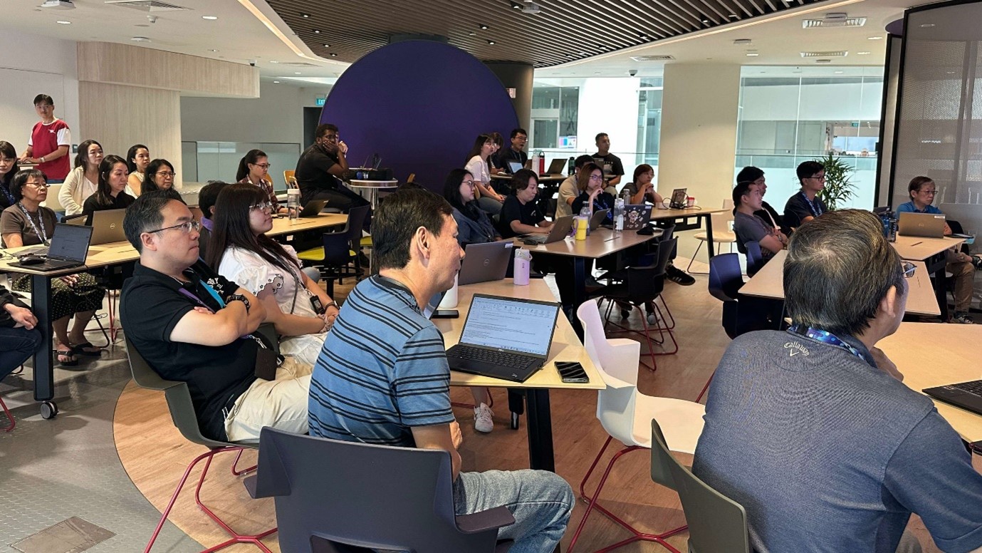 A group of people sitting in a room, facing the front, with laptops in front of them.