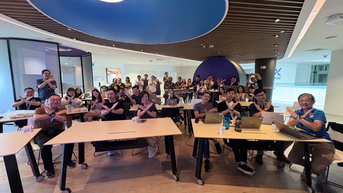 A group of people sitting at tables and posing with their hands forming an 'X'.