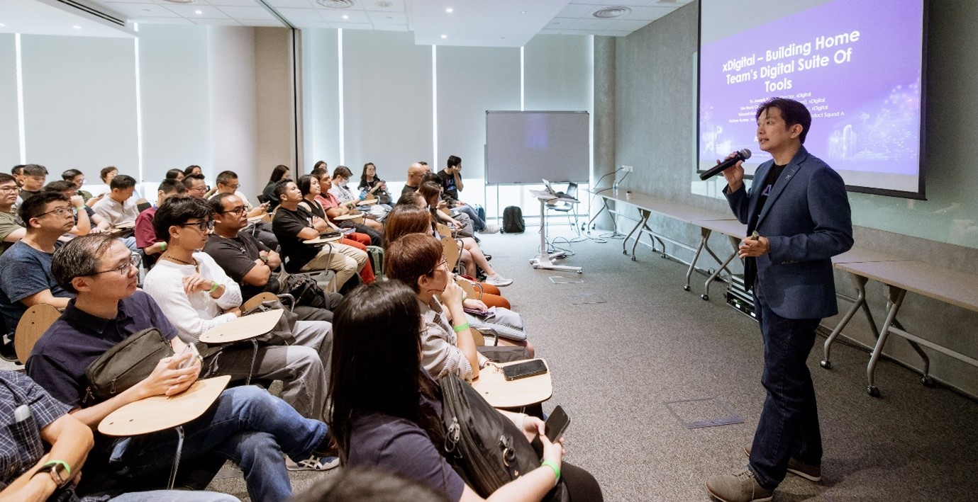 A standing man speaking to a seated audience.