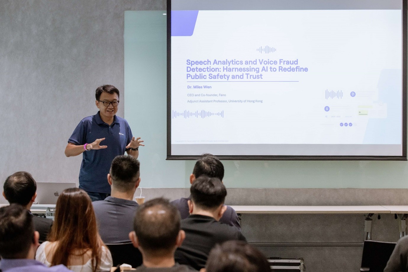 A standing man speaking to a seated audience.