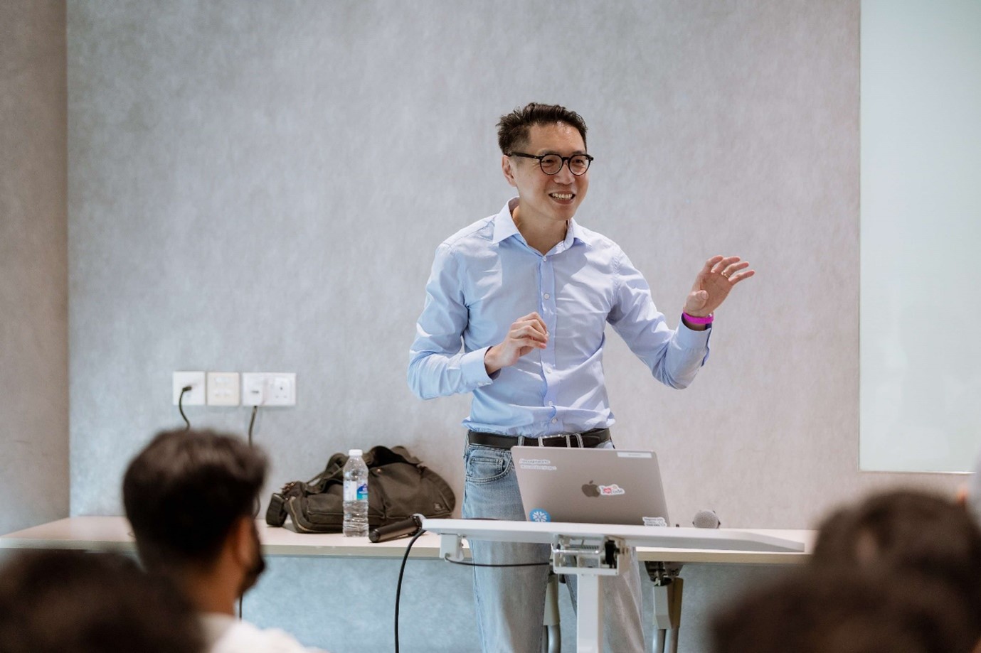 A standing man speaking to a seated audience.