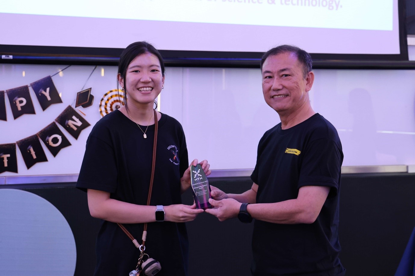 A female receiving a glass trophy from a male.