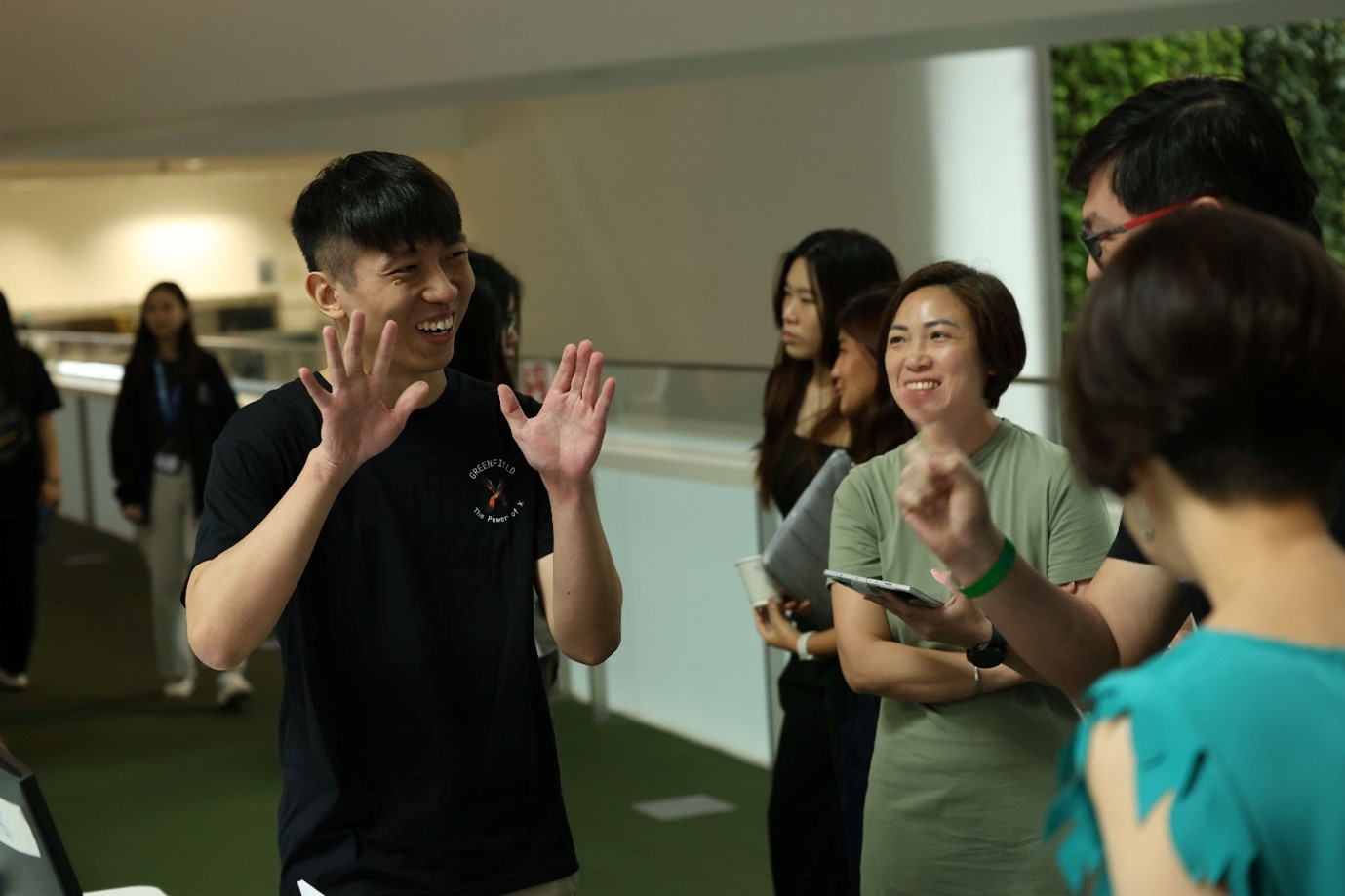 A male gesturing with both palms up as he smiles and speaks to a group of people.