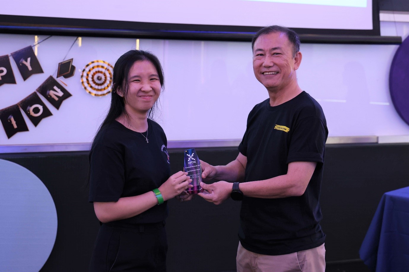 A female receiving a glass trophy from a male.