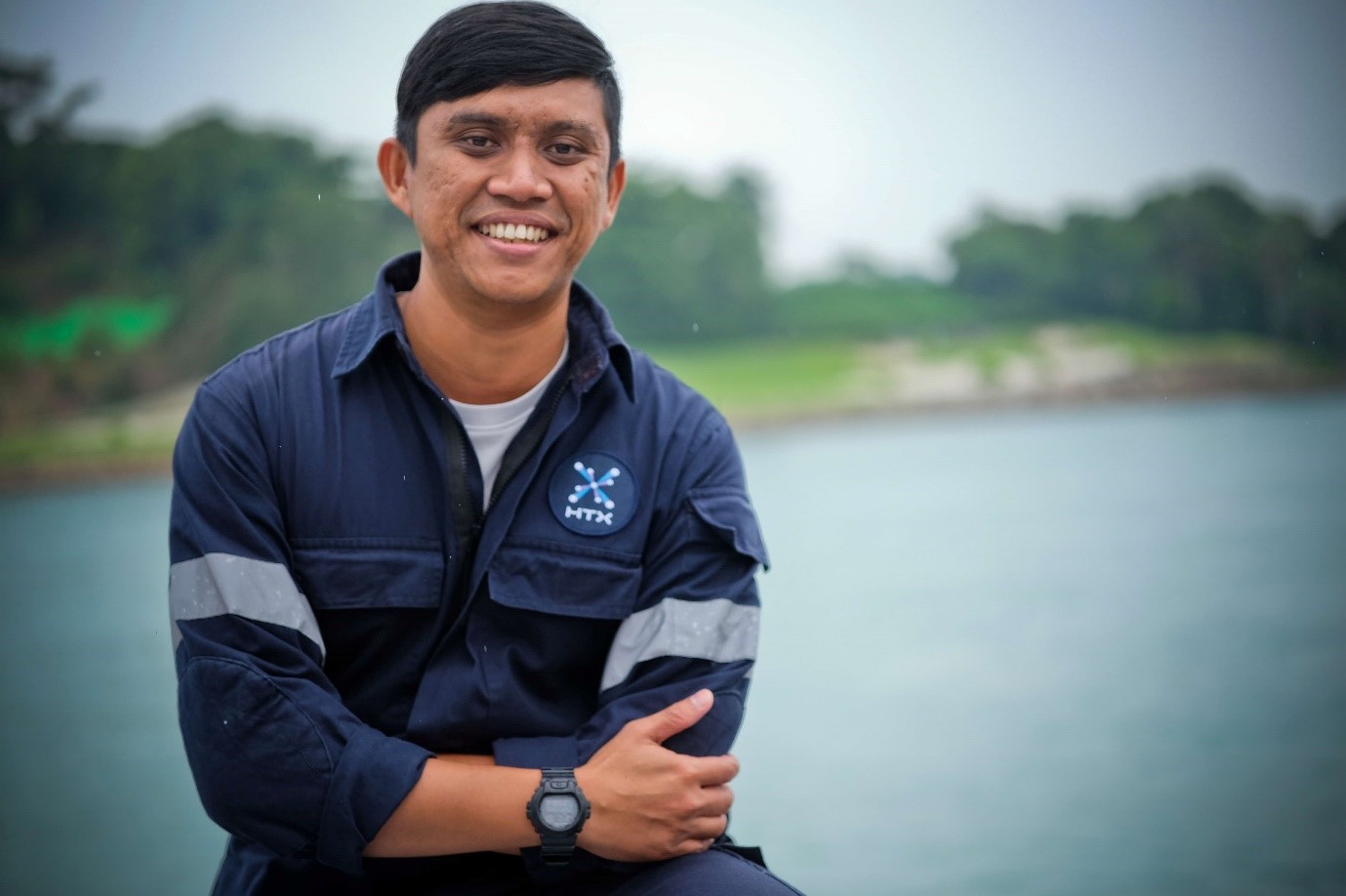 A man in coveralls smiles with his arms folded.