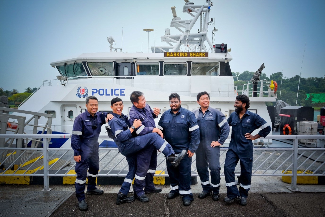 A group of men in coveralls pose in front of a boat.
