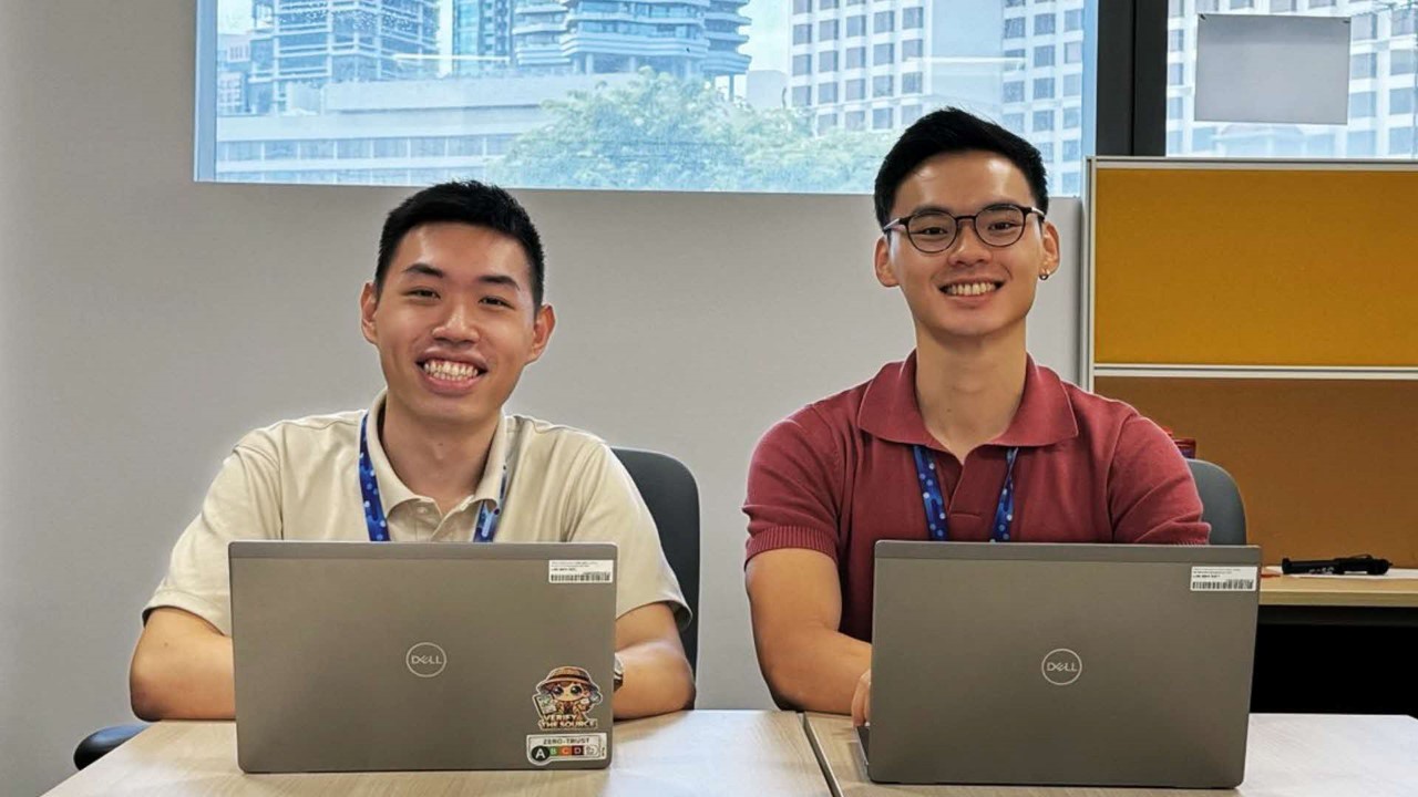 Two men sitting at a table with laptops smiling.