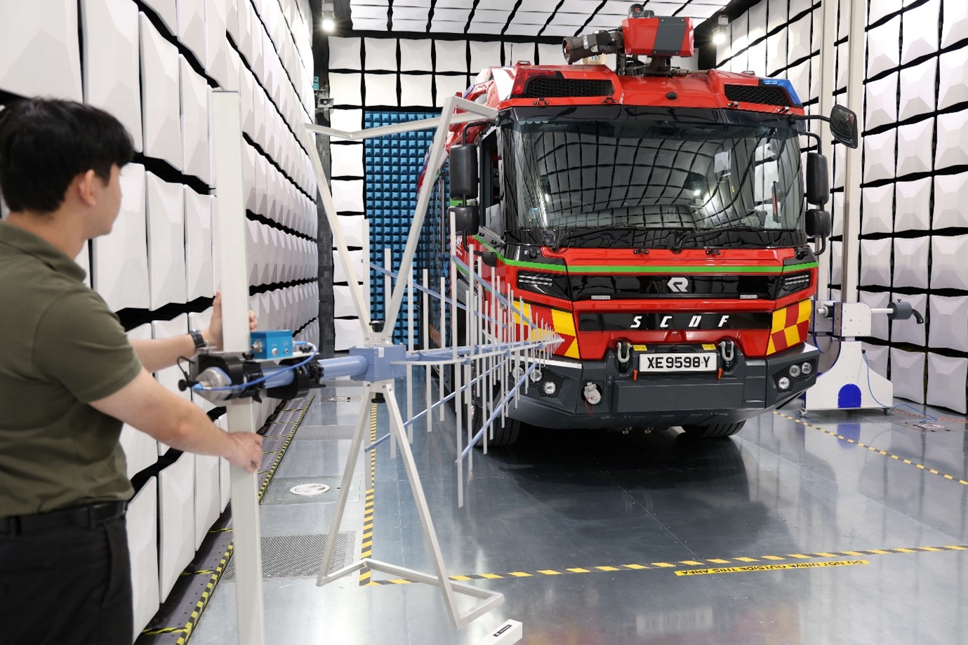 A person standing in a room with white tiles and holding an equipment pointed at a large red truck.