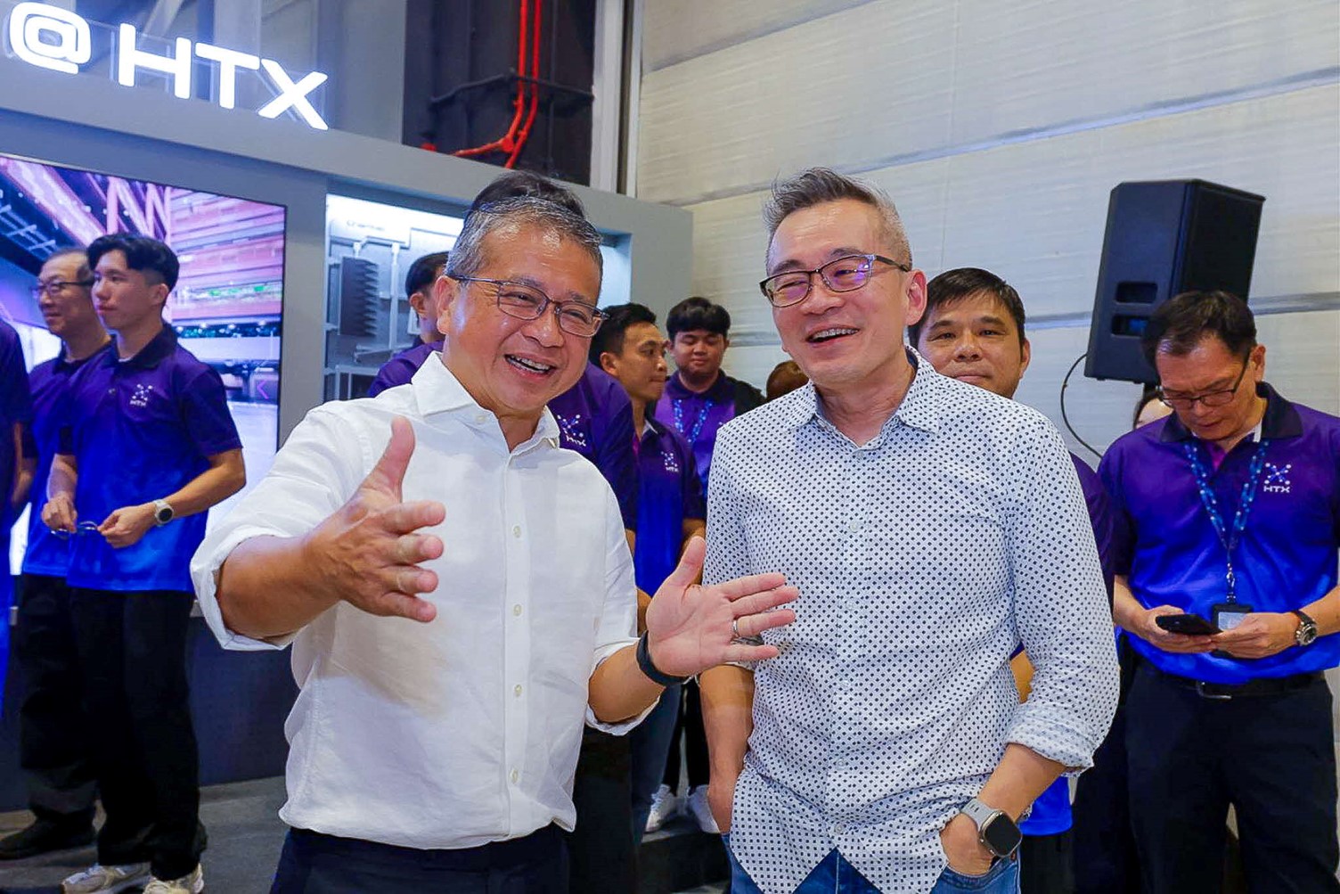 Two men smiling and talking while standing in a crowded room.