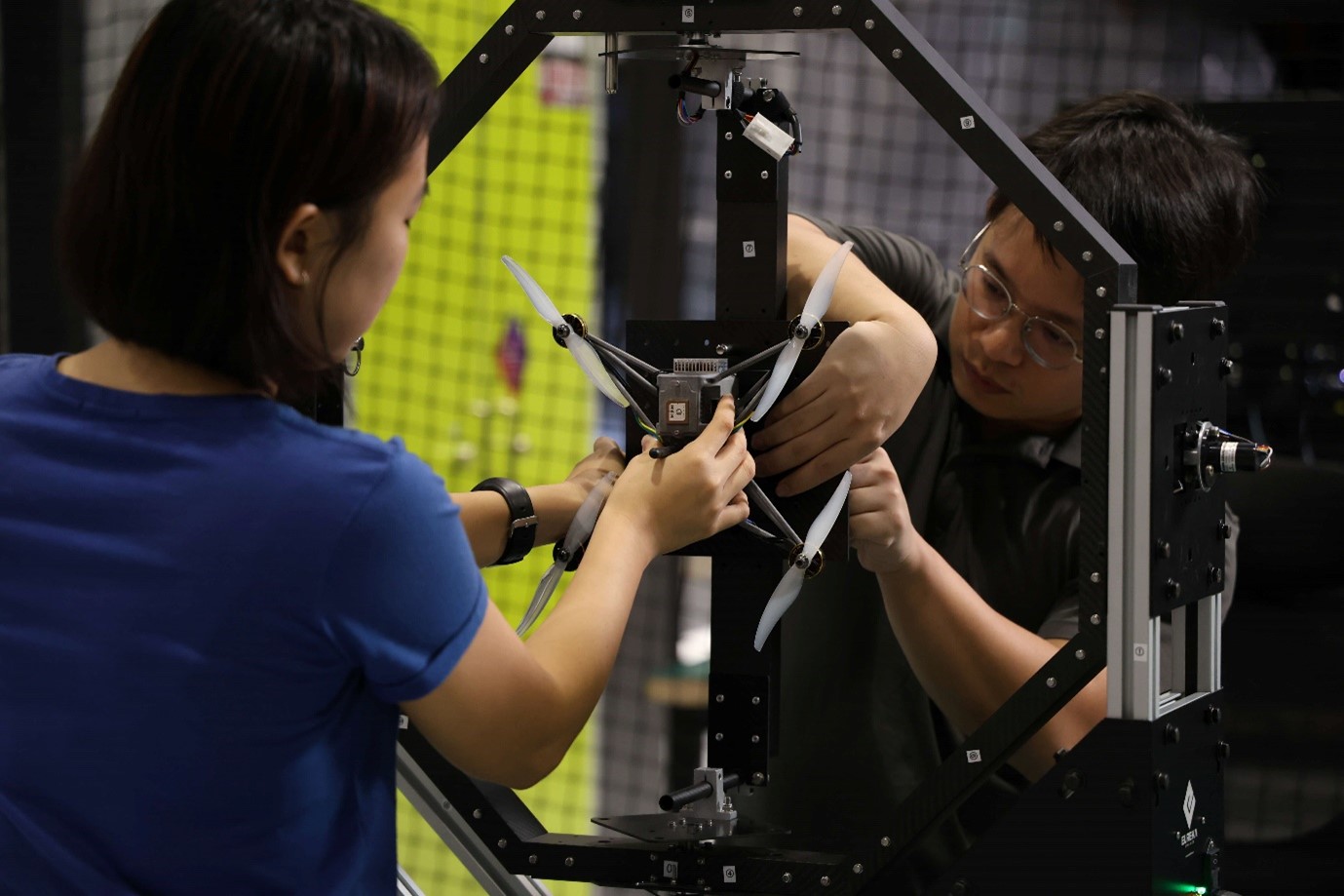 A female and male work on attaching a drone to a large hexagonal frame.