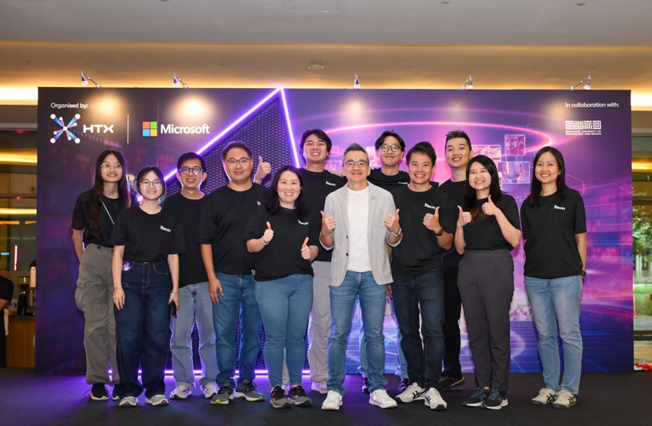 A group of people pose for a photo against the HacX event backdrop.