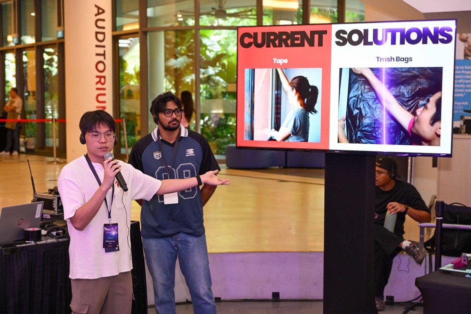 A man presents in front of a screen, speaking into a microphone.