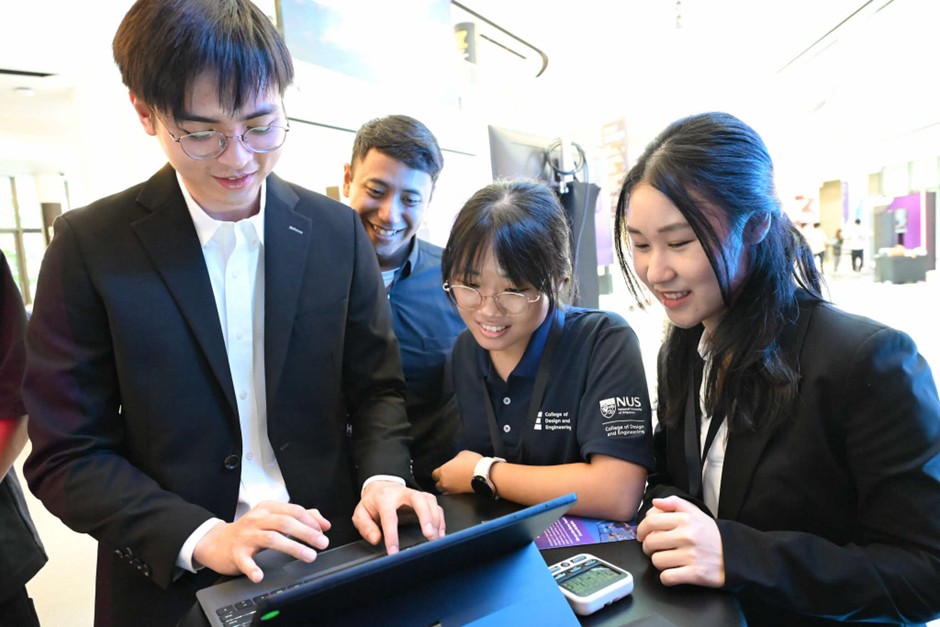 Four people look at a laptop screen together.