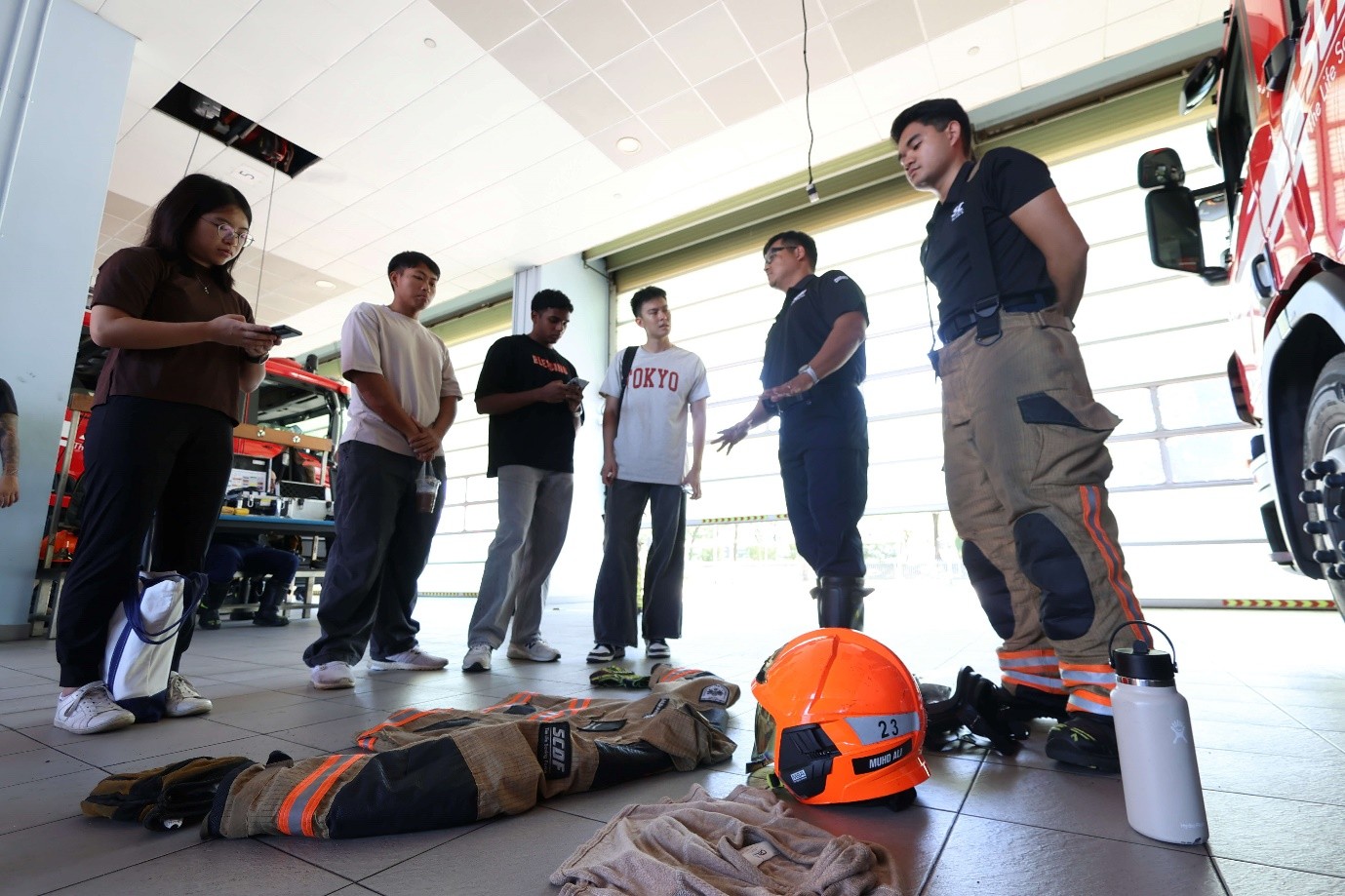 A group of people talking and standing around firefighting equipment laid on the floor.