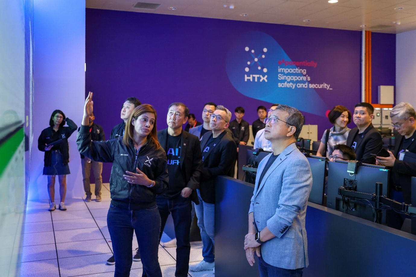 A woman presents to Mr Tong during a tour of HTSC, with HTX’s logo and tagline visible in the background.