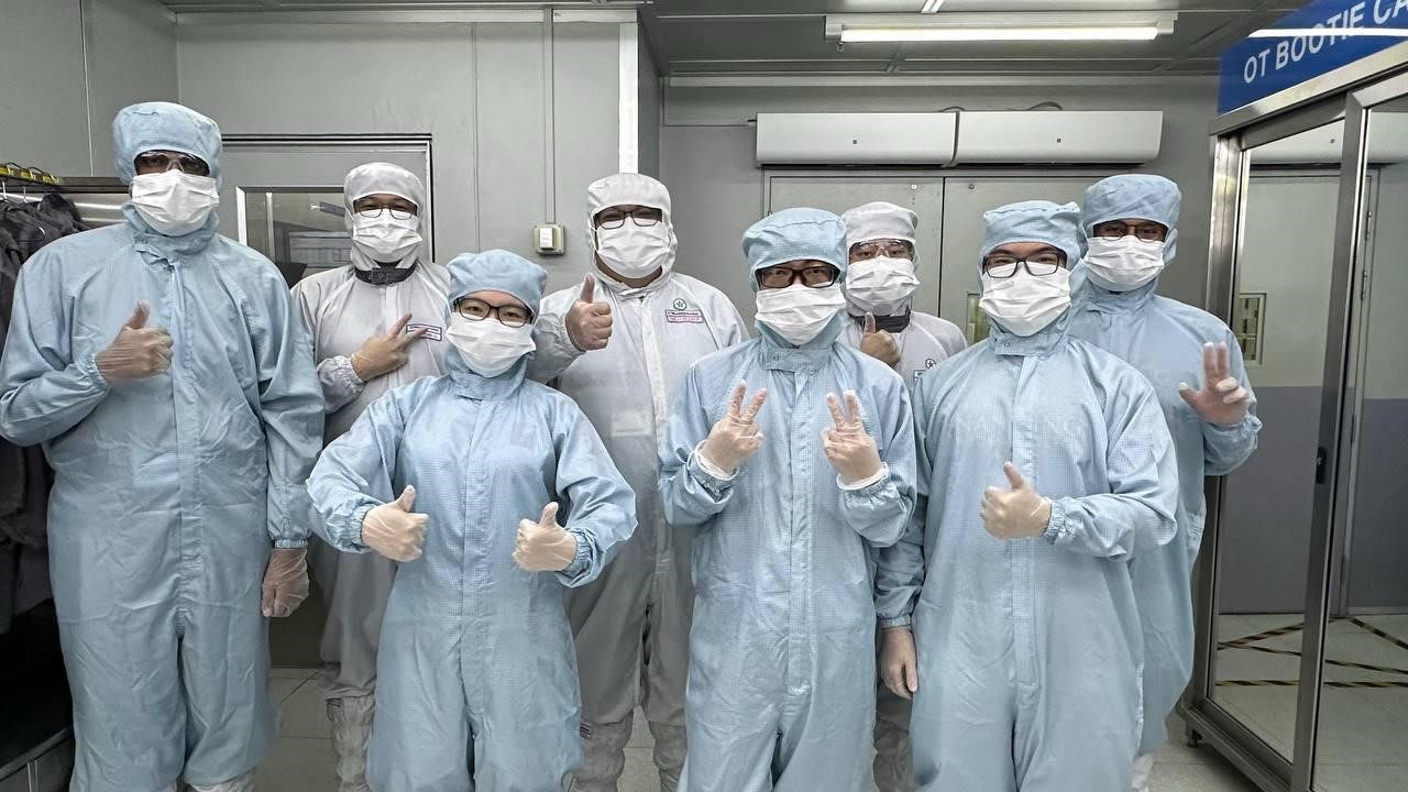 A group of eight people in cleanroom suits and masks posing.