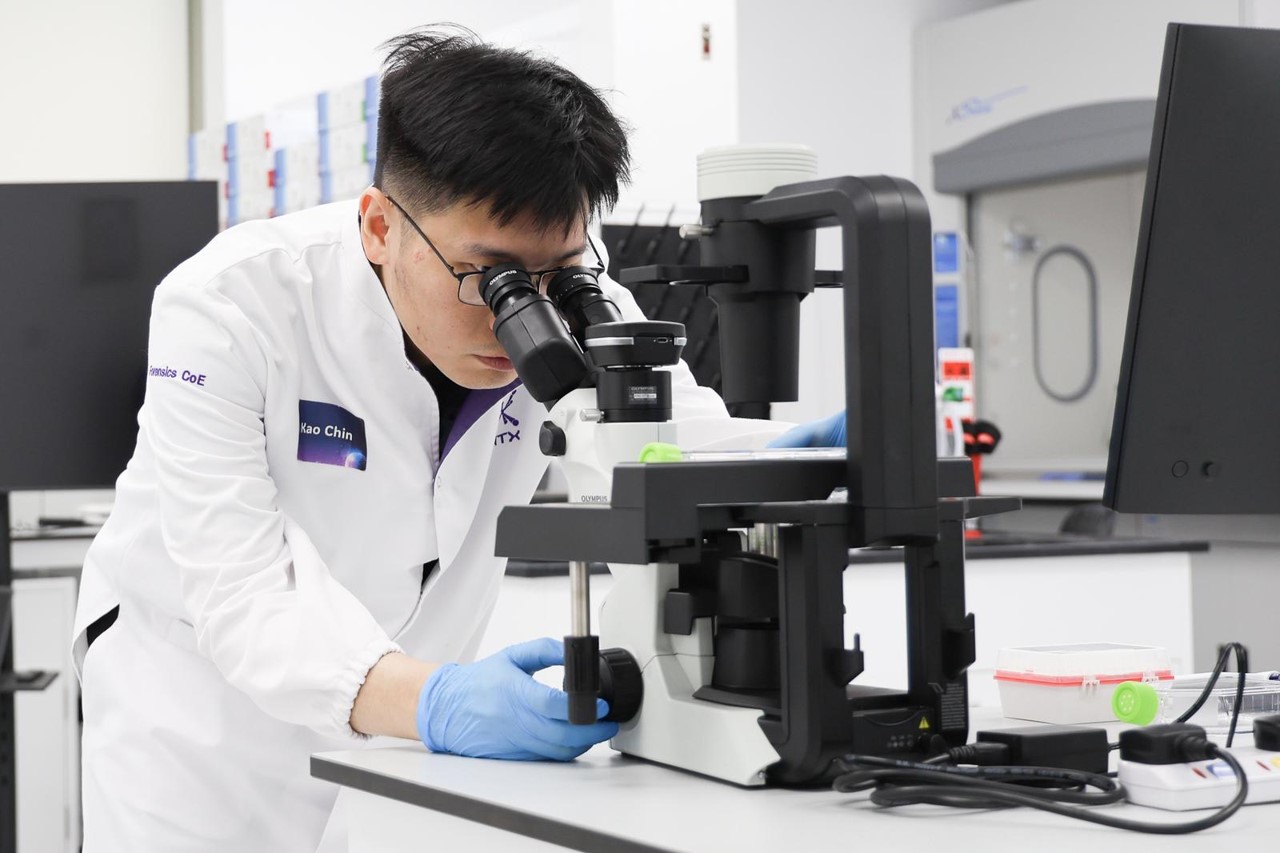 Scientist in lab coat and gloves using a microscope in a laboratory, focusing intently on a sample.