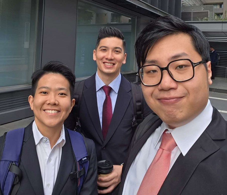 A group selfie of three smiling individuals in suits.