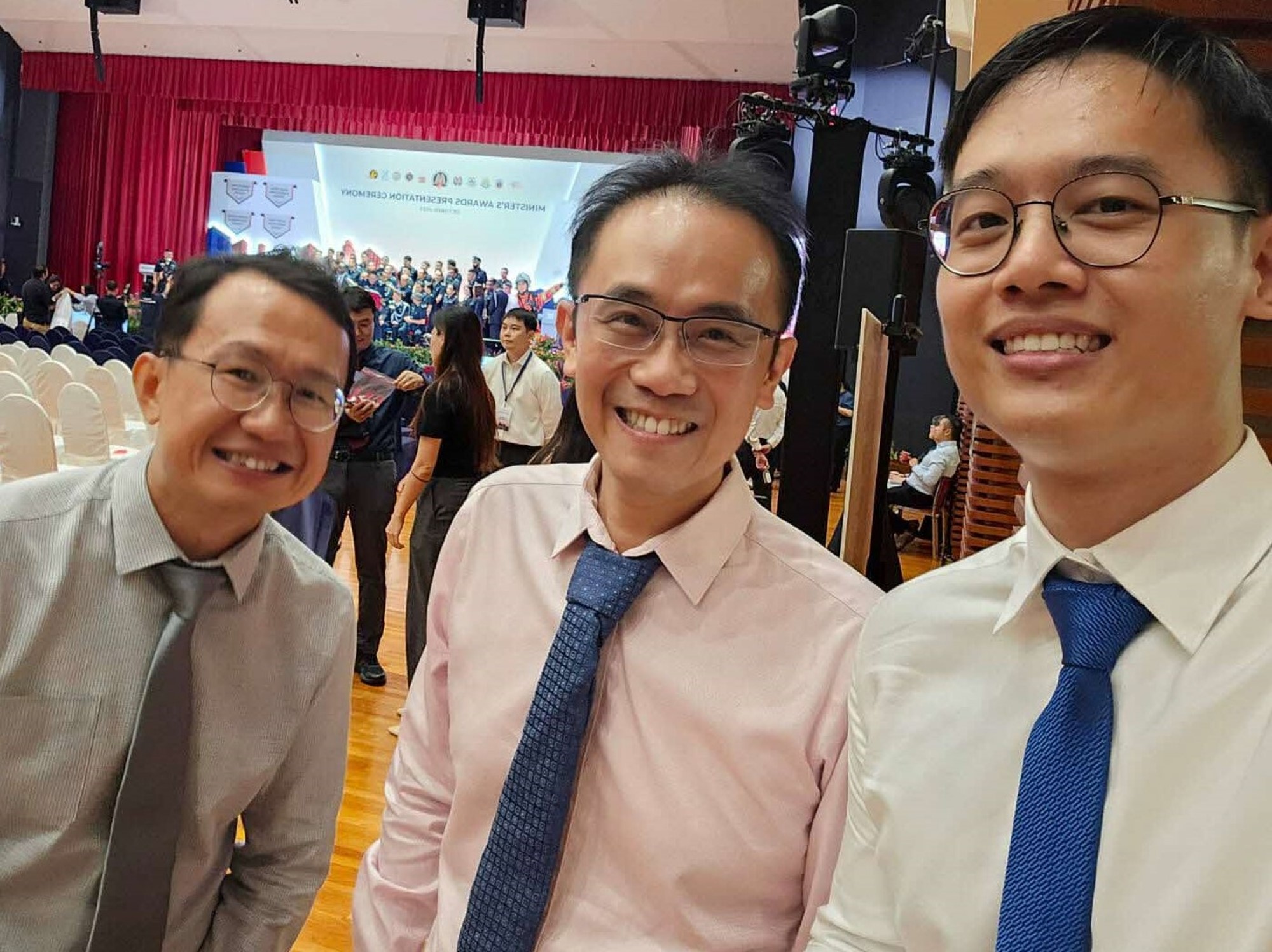 Selfie of three men smiling indoors at an event.