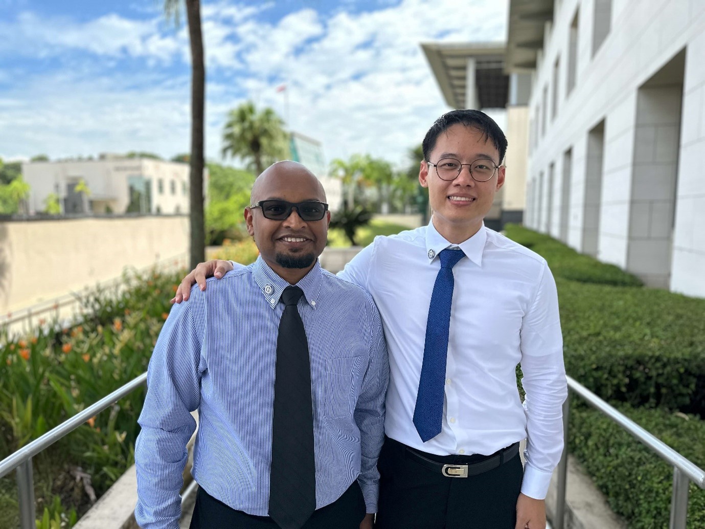 Two men in shirts and ties standing outdoors, smiling at the camera.