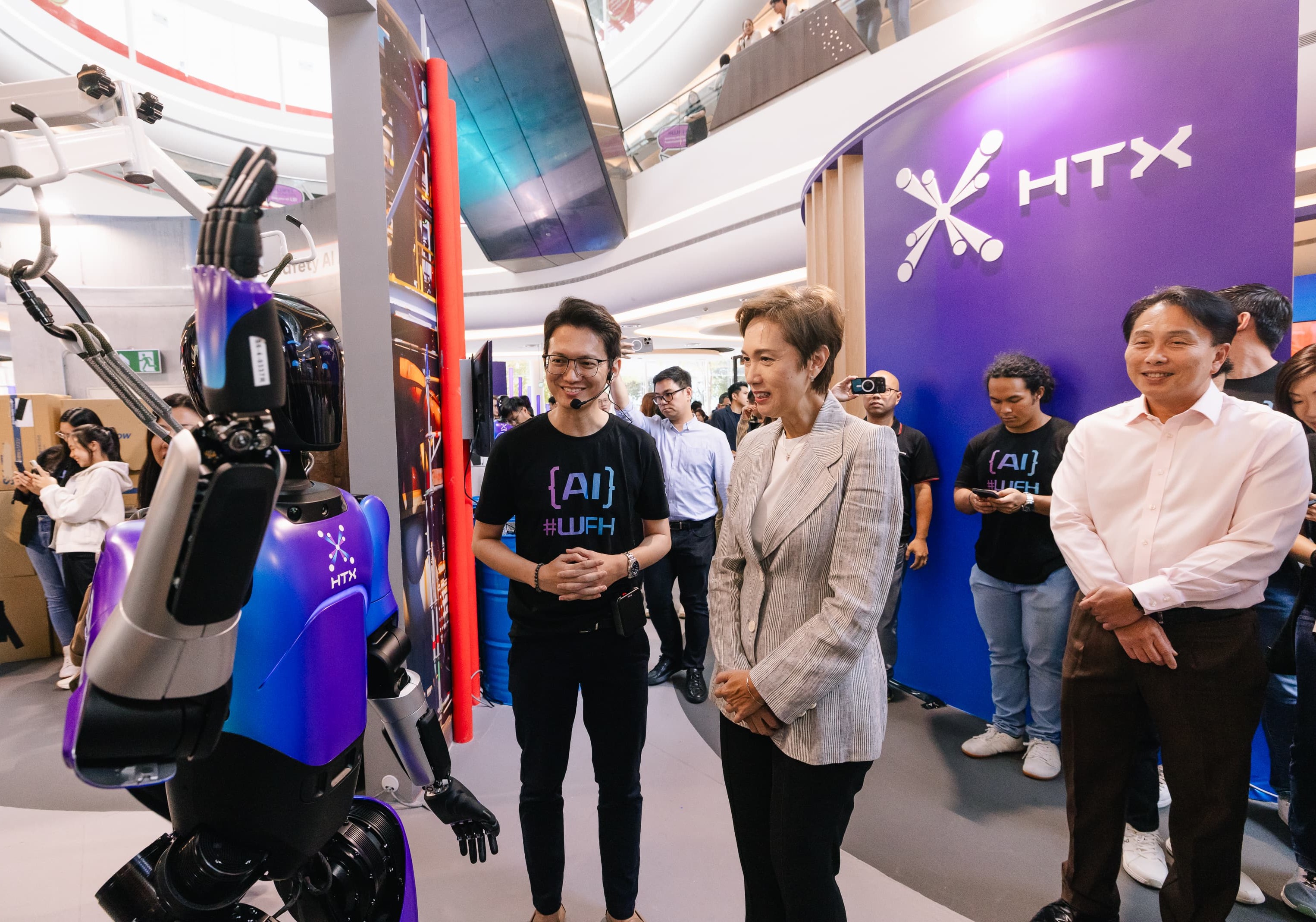 A humanoid robot with the HTX logo interacts with a group of people at a technology exhibition.