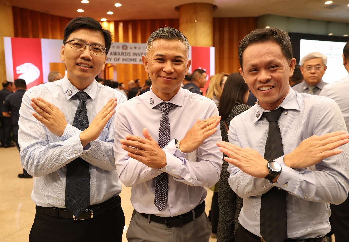 Three men in formal wear smile and pose with their arms crossed in an X shape.