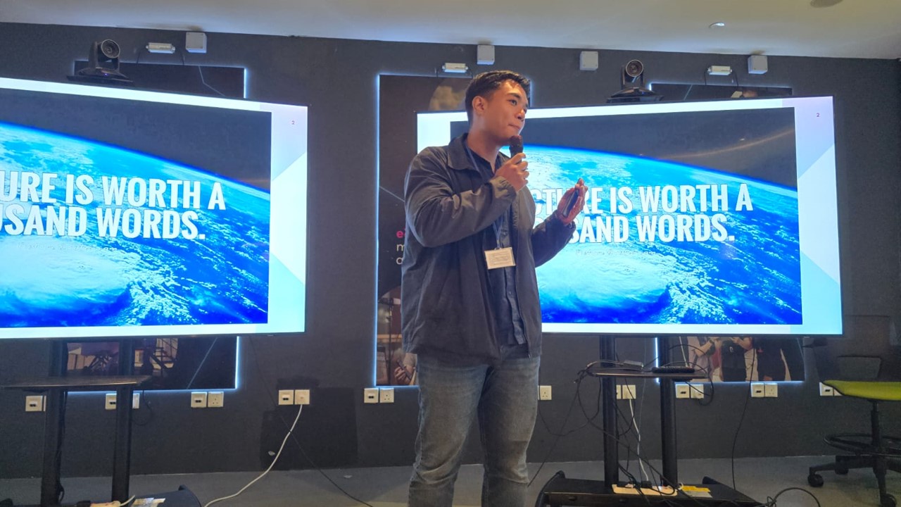 A man presenting on stage with a microphone in front of a large screen showing “A picture is worth a thousand words.”