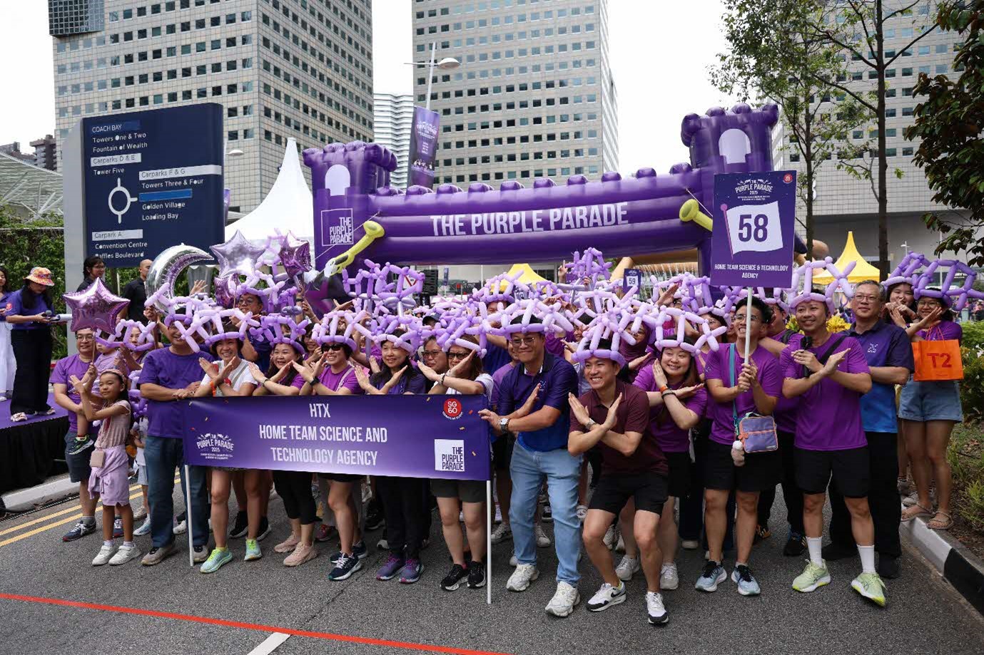 A large group of people holding a banner, wearing balloon hats and crossing their arms in an X pose.