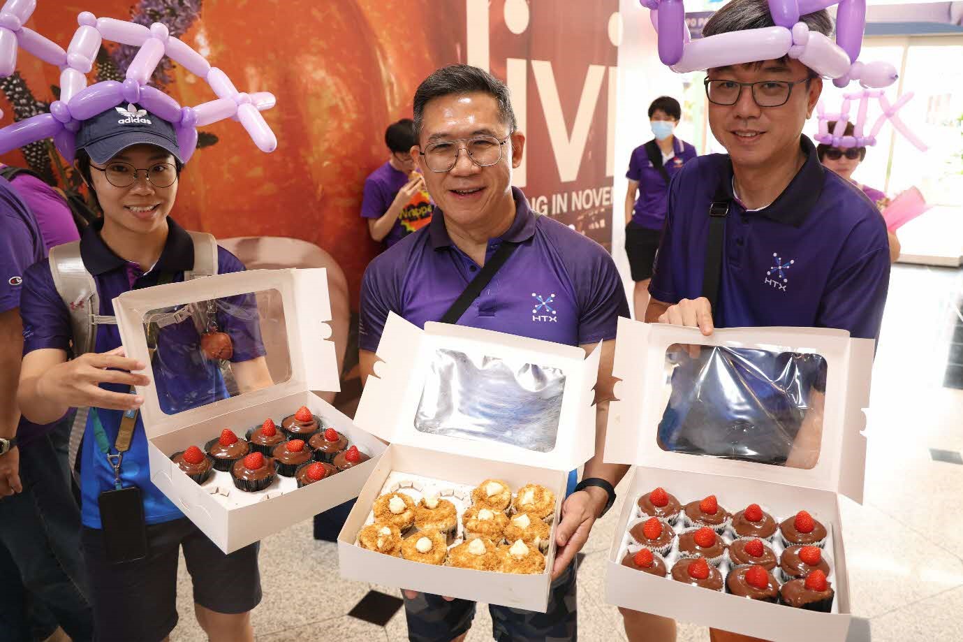A group of three people holding boxes of cupcakes.