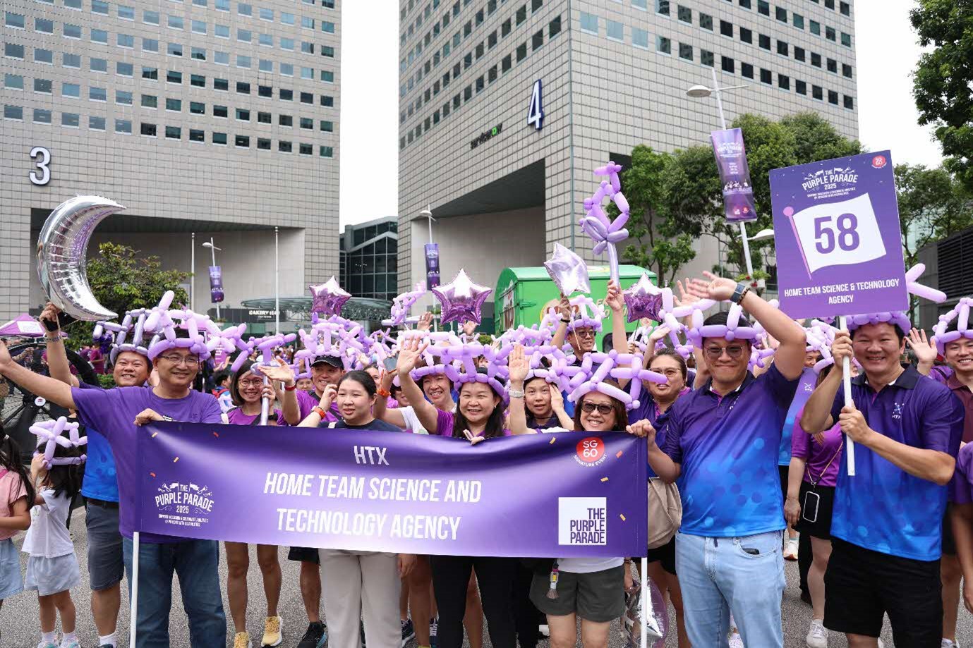 A large group of people holding a banner and wearing purple balloon hats and waving.