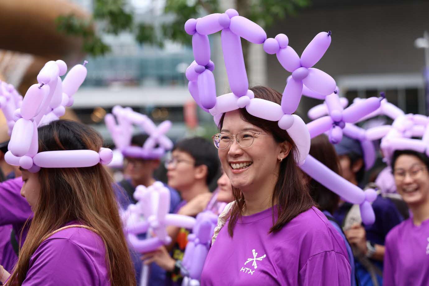 A lady smiles amidst a group of people wearing purple balloon hats.