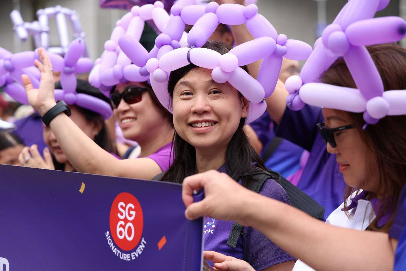 A lady smiles to the camera amidst a group of people wearing balloon hats.