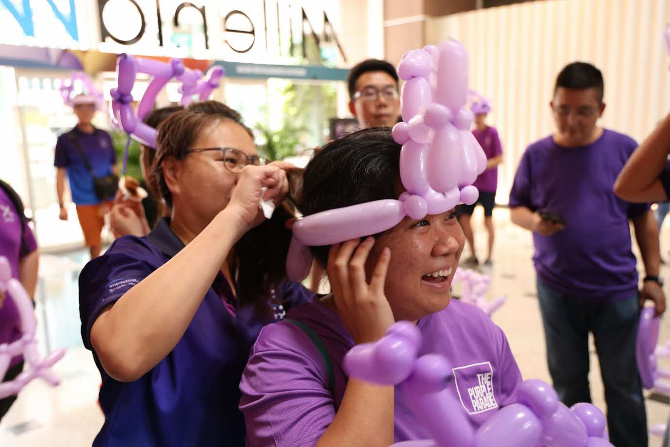 A person puts a balloon hat on another.