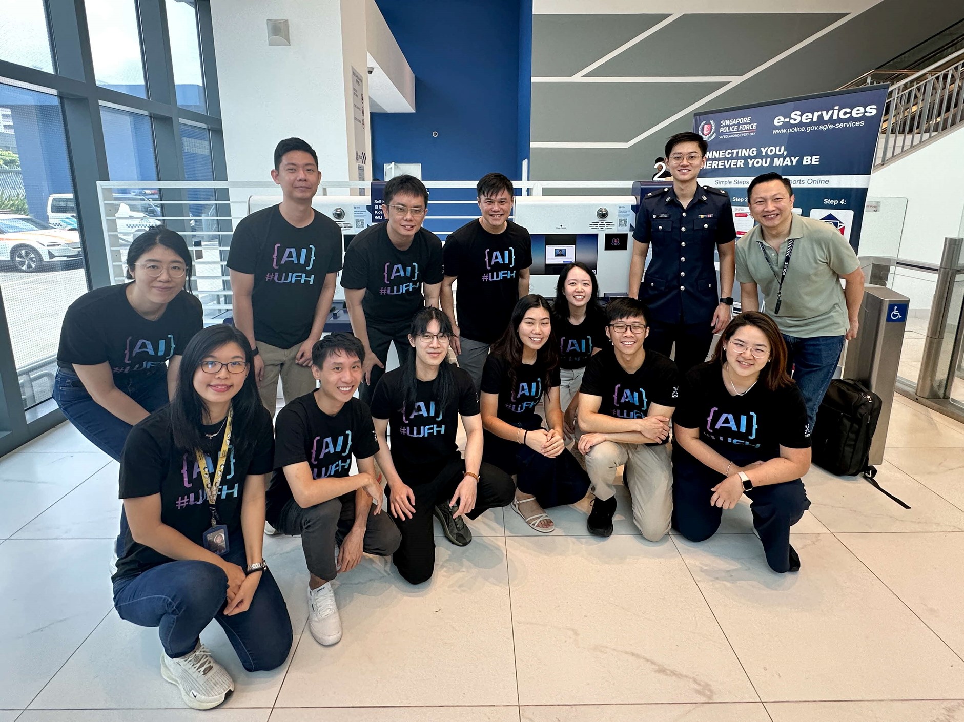 Group photo of 13 people, mostly wearing matching black shirts, posing near a self-help kiosk.