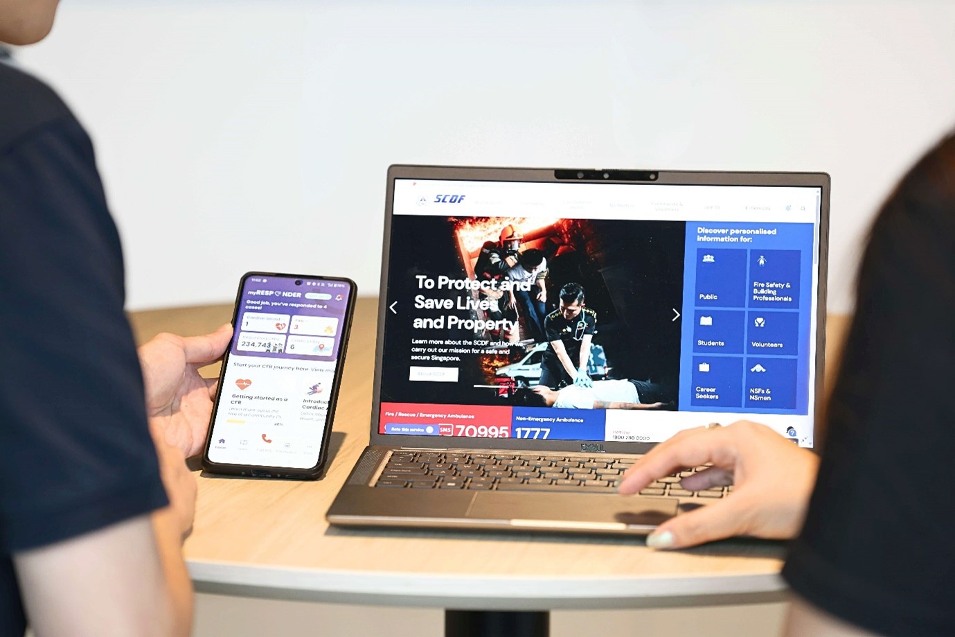 A person holding a smartphone with the MyResponder app open, next to a person using a laptop displaying the SCDF website.