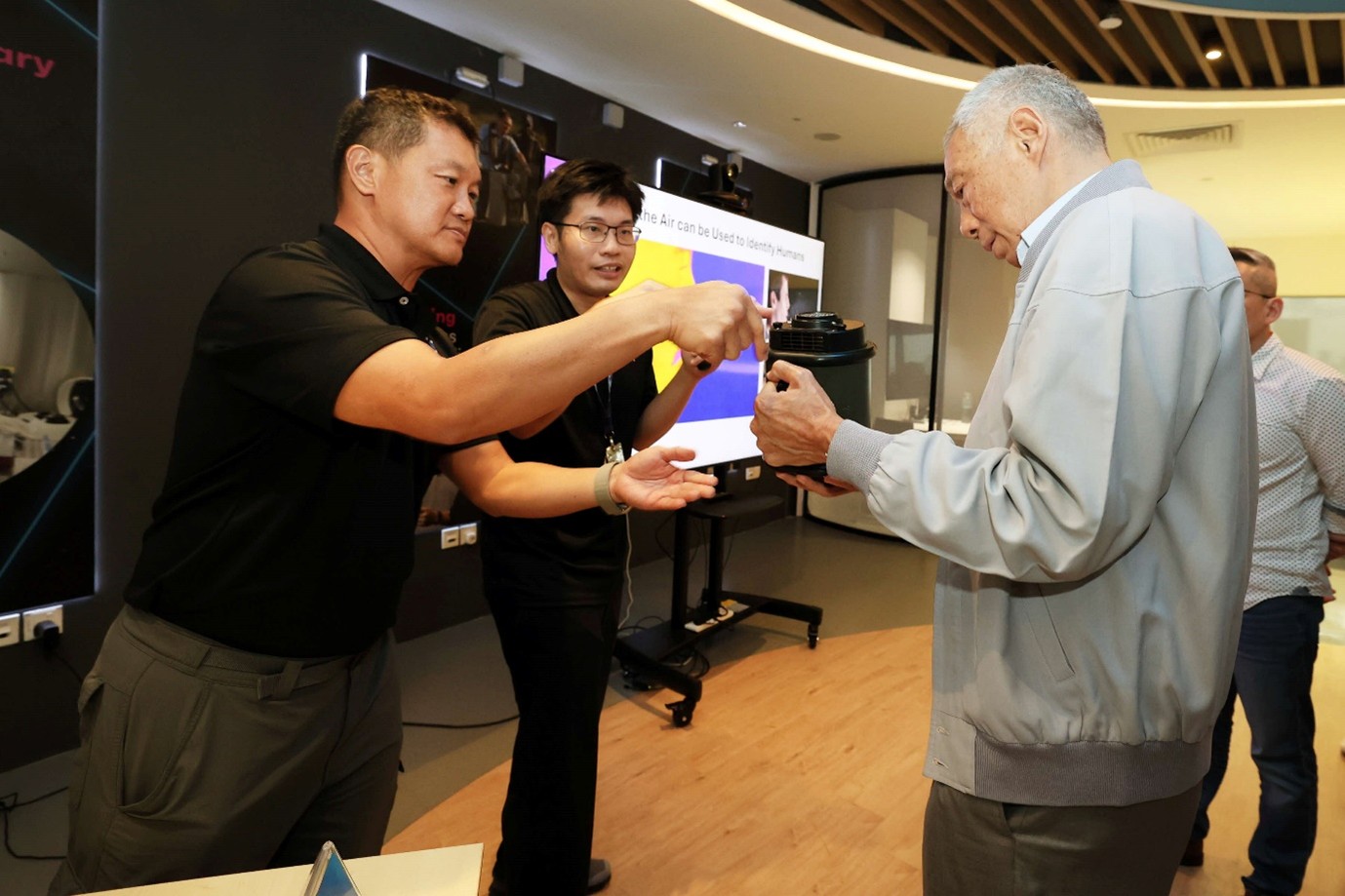 Two men gesture towards an equipment held by another man.