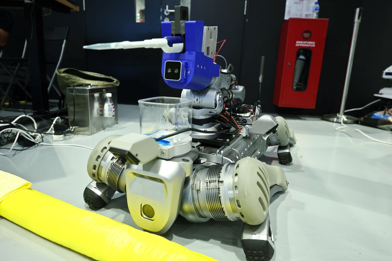 A robot dog on a floor with an arm attached on top with a pipette.