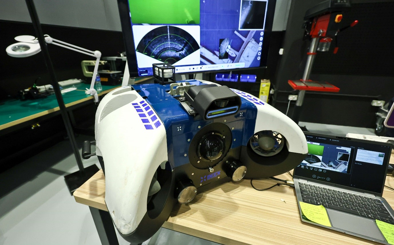 A machine on a table next to a laptop and in front of a TV screen showing scan images.