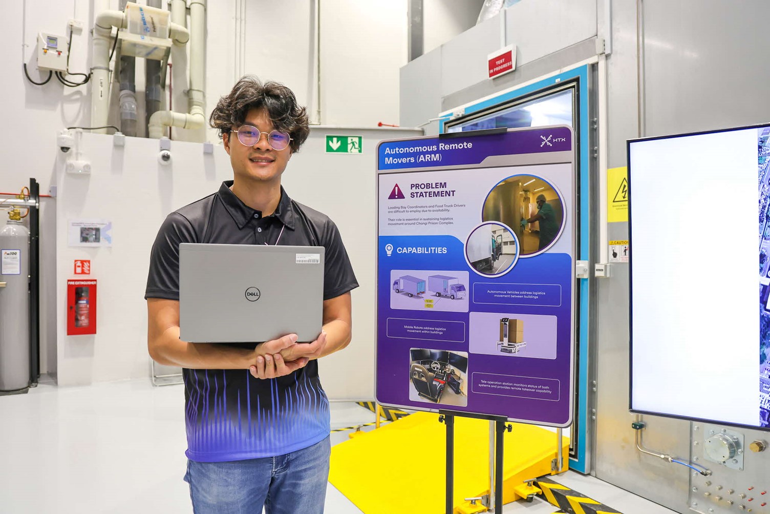 A man holding a computer and standing in front of a poster and screen.