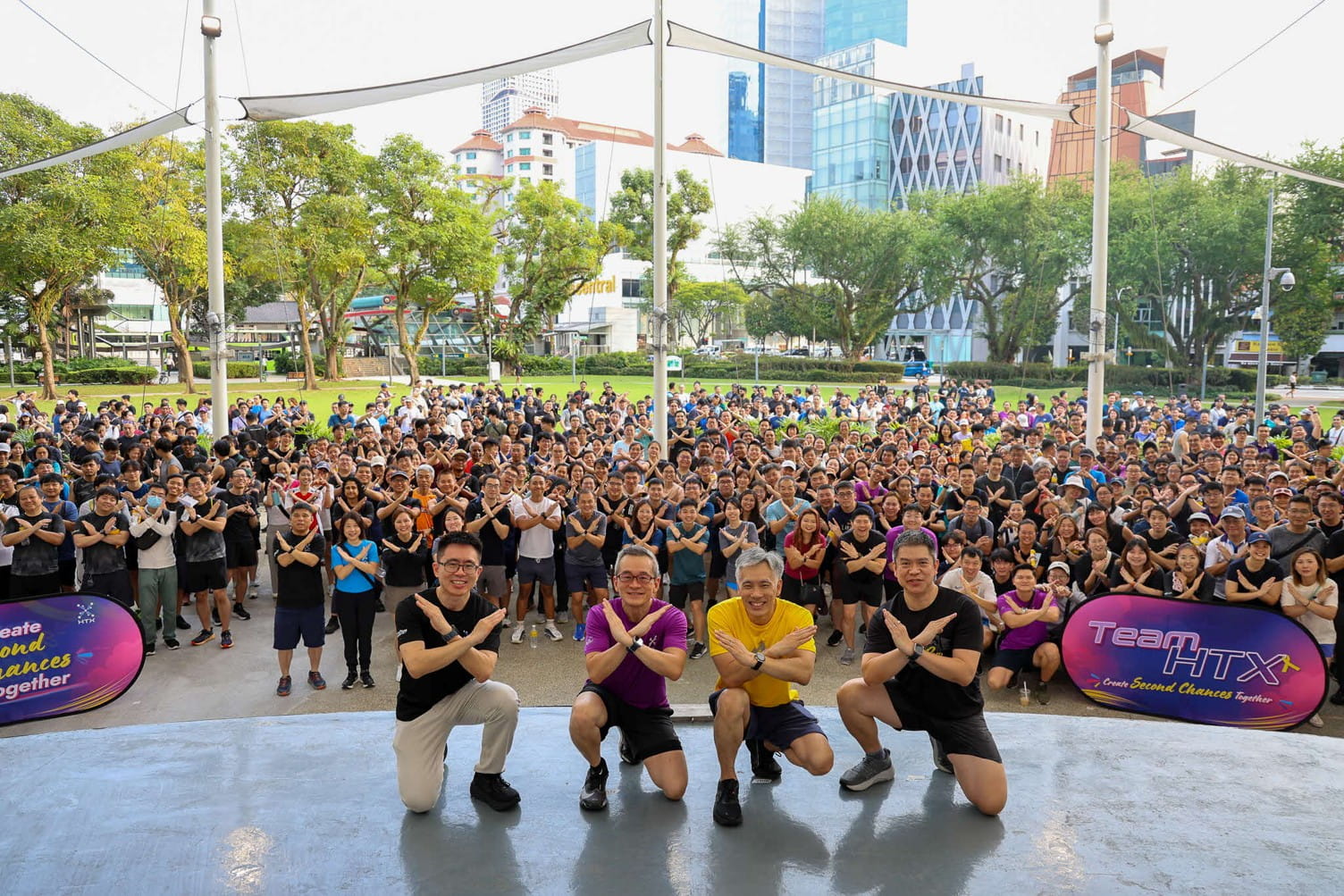 Large outdoor fitness event group posing in front of urban parks and high-rise buildings.