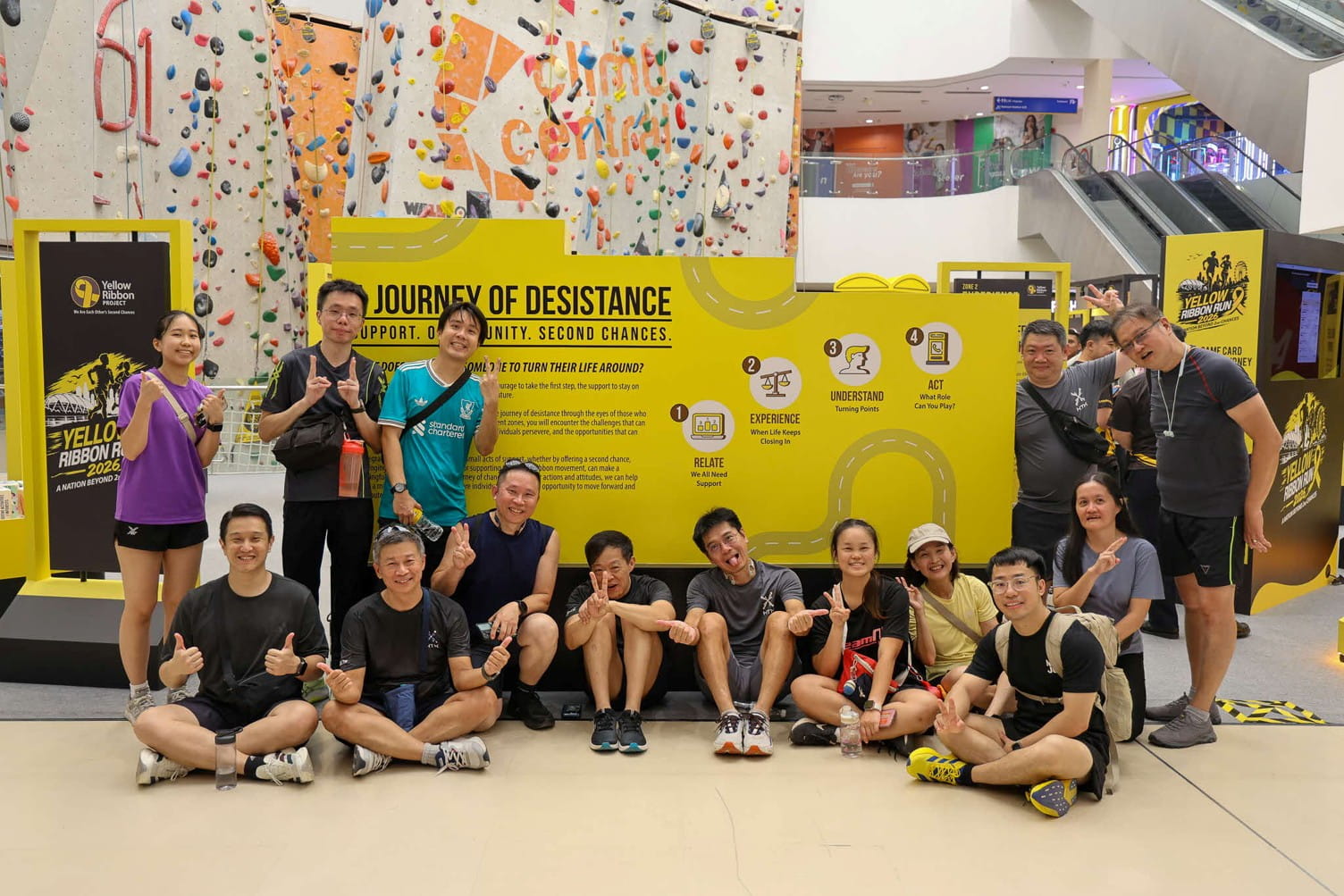 Group posing beside a yellow “Journey of Desistance” informational display indoors.