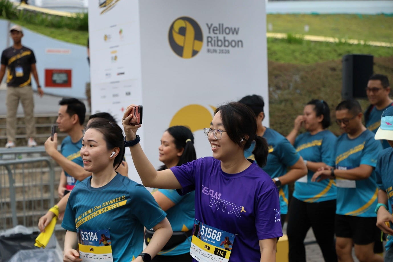 Runners in event shirts and numbered race bibs near a Yellow Ribbon sign.