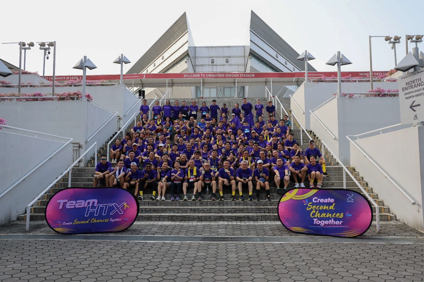 Large group in purple shirts gathered on stadium steps for a photo at Singapore Indoor Stadium.