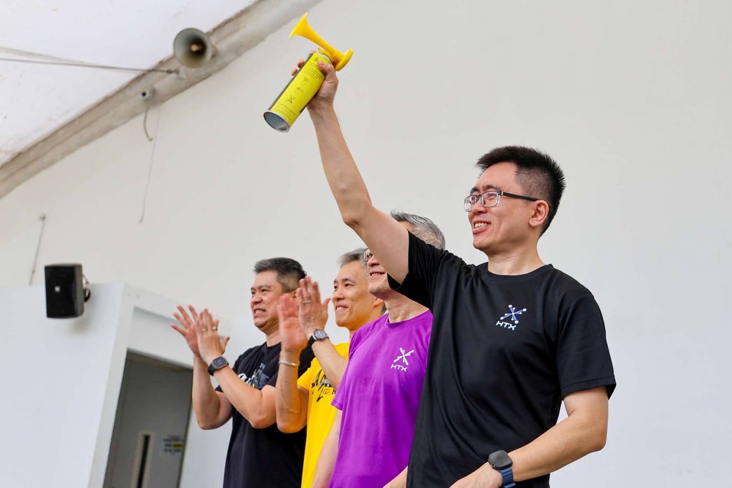 Four men celebrating, with one raising a yellow handheld horn.