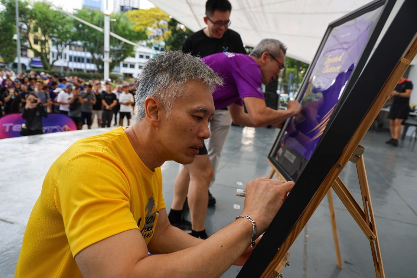 Two men signing on shirts in a display frame.