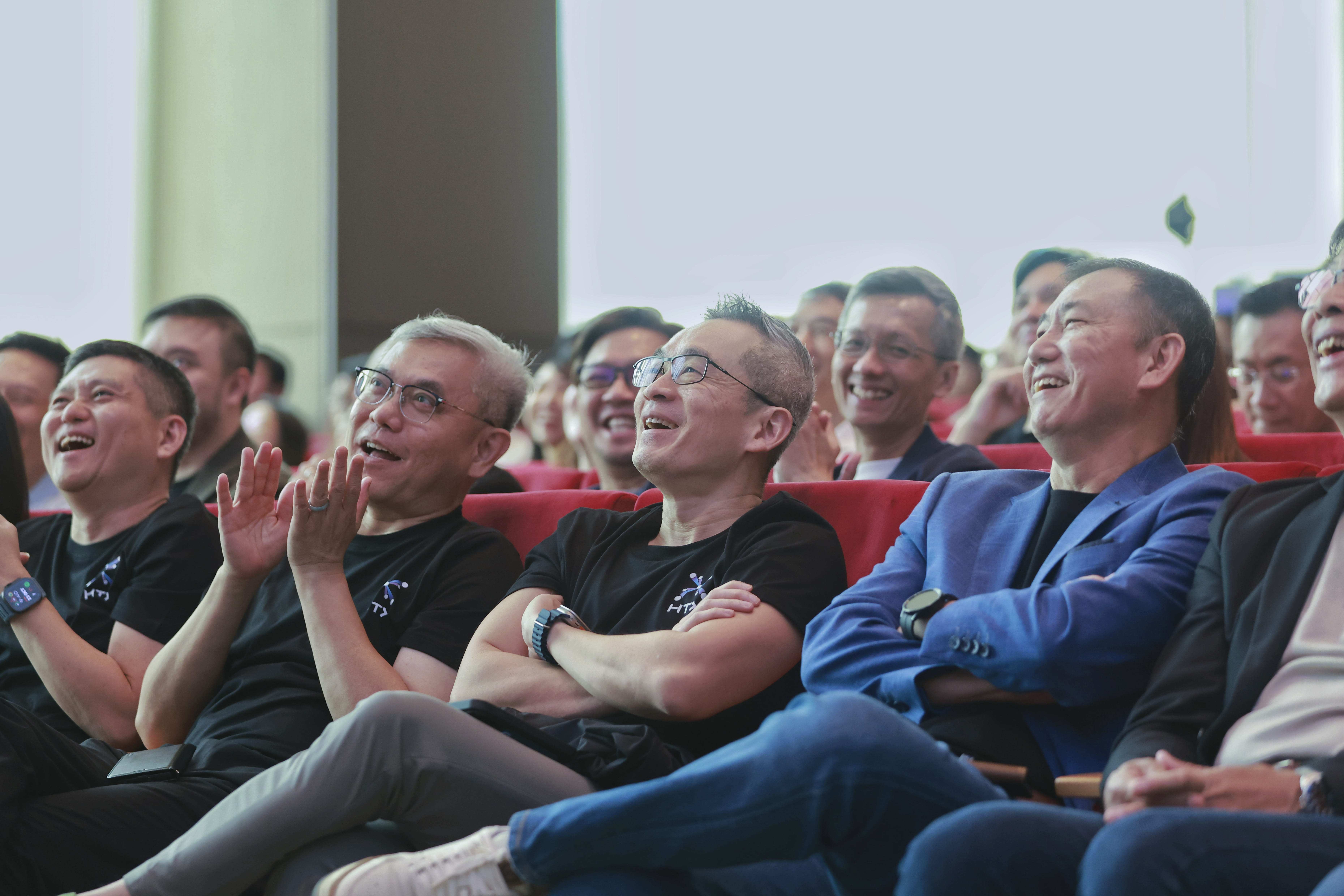Audience seated in auditorium chairs smiling.