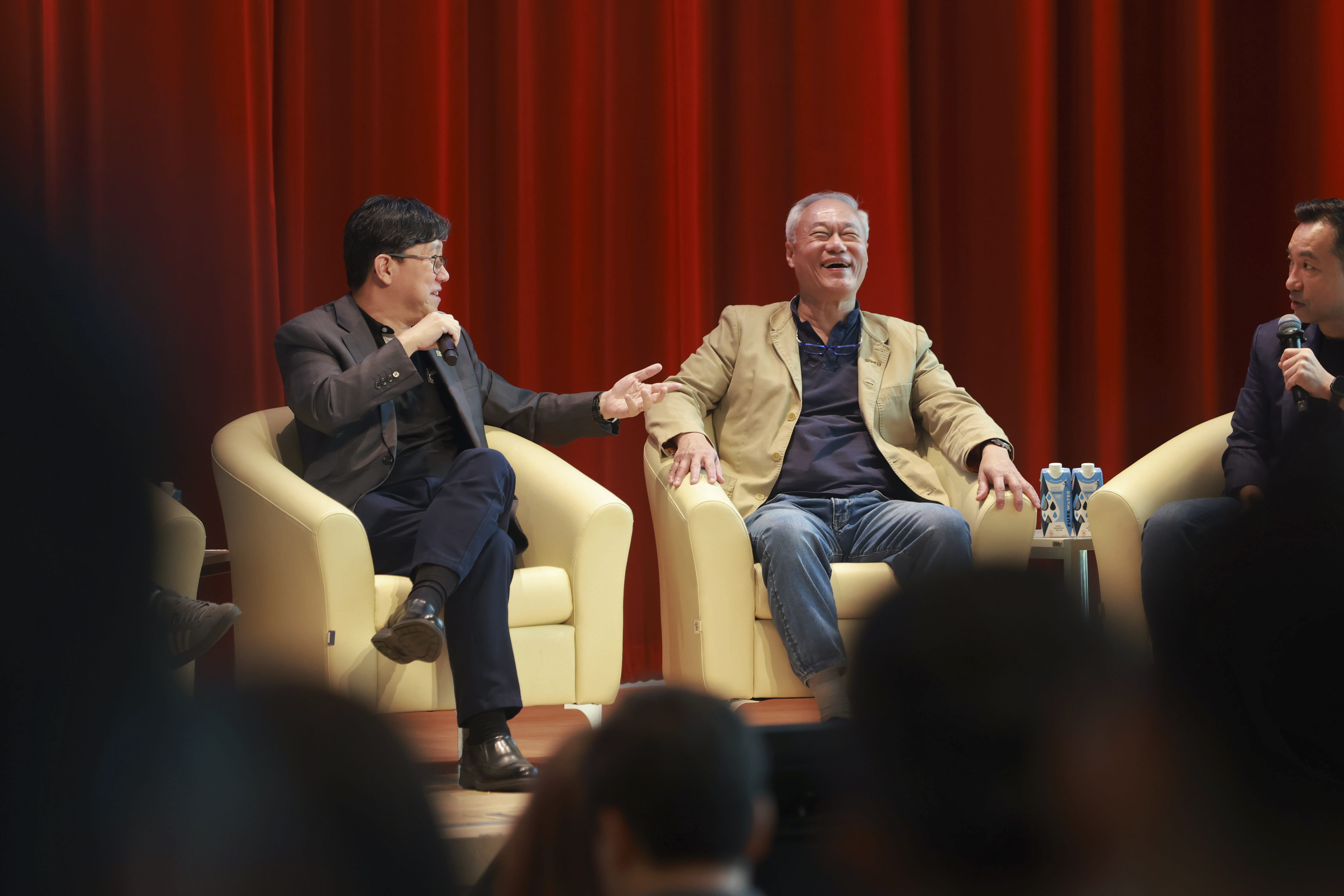 Three men in a panel discussion on stage before a seated audience.